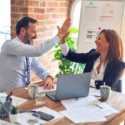 businessman and businesswoman sitting at a desk giving a high five