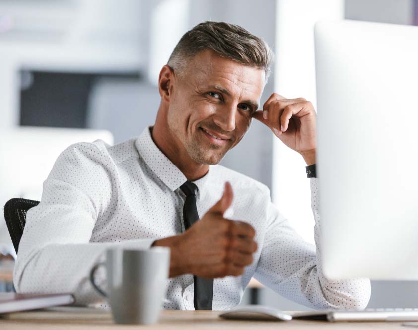 smiling business person with right thumb up in front of a desktop screen